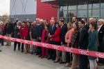 Group of people cutting a red ribbon in front of building