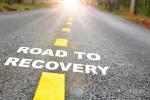 A paved road with yellow lines in a forest with the words ROAD TO RECOVERY.