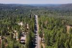 Aerial view of a rural Northern California highway surrounded by dense pine forest and scattered homes under a clear blue sky
