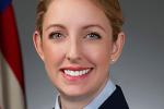 Blonde woman in Air Force uniform, light blue shirt, dark blue blazer and American flag in the background.