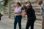 Woman facing cinematographer’s camera being interviewed by film crew