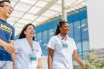  A smiling male medical student wearing a blue t-shirt walks with two smiling female nursing students dressed in white topped scrubs