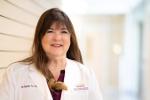 Deb Bakerjian stands smiling while wearing her white clinical coa