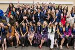 nursing graduates sit and stand in three rows side-by-side with arms in the air celebrating