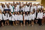 physician assistant students wearing white coats stand side by side smiling in front of stage