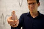 Man with brown hair and navy long sleeve shirt holds a rectangular plastic slide which in turn holds a small square probe.