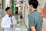 A doctor in a white coat uses hand gestures to instruct a medical student in scrubs in the hallway of a pediatric clinic.