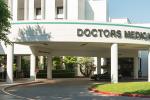 A white, multi-story building that has an overhang in the front that reads in dark letters, “Doctors Medical Center”