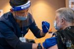 Nurse wearing mask and face shield injecting vaccination in person arm with sleeve rolled up. 