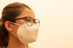 Worried-looking woman wears a mask against a hazy pink background of bad air.
