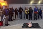 Woman demonstrates how to use AED on a mannequin as a dozen people watch.