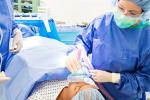 A young patient is being sedated while laying on operating table. A female anesthesiologist is using medical equipment to sedate patient.