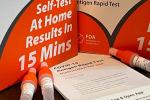 two orange ihealh COVID test kit boxes on a countertop with three vials of liquid and testing instructions