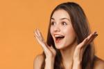 Surprised, happy woman with long hair smiles with open hands near her cheeks. 