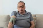 Older man sitting on a couch in a living room measuring his blood pressure 