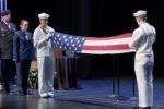 A military color guard of four uniformed members of the armed services stands on stage and folds the U.S. flag
