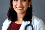 A young woman with dark hair past her shoulders, red wine-colored top and white lab coat, and stethoscope around her neck