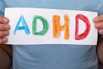 Torso of a young boy in a blue shirt holding a sign that says “ADHD” in crayon.