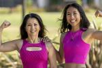 Two women in pink outfits flexing their arms, symbolizing strength and support for breast cancer awareness.