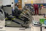 Three people sitting on exercise bikes in exercise room with three people in medical scrubs standing in the back of the room.