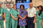 Six people standing in a row in an operating room with computer screens above their head. 