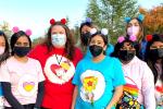 : A group of eight women wearing pink, blue and red Care Bears T-shirts and wearing headbands with fuzzy bear ears - group photo outside at dusk