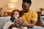 Man holds child with breathing device around nose and mouth.