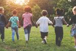 A diverse group of young children run across a field while holding hands.