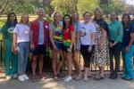 A dozen adults stand side-by-side along a fence at a park. 