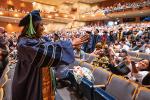 A female medical student in blue gown and cap gestures to supporters in the audience of Mondavi Center during Commencement 2022