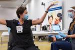 A nurse in blue scrubs throws her hands in the air jubilantly after getting a COVID shot