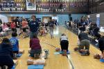 Six participants practice hands-on CPR on dummies on the floor of a gymnasium