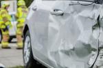 Damaged gray car with three firefighters wearing yellow jackets in the background.