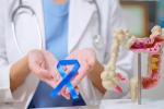 Doctor holds blue ribbon in their hands. Plastic mold of intestines is on a desk next to them. 