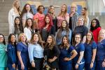 22 women stand in three rows indoors