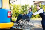 Driver helping a man on wheelchair getting into taxi