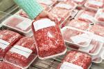 Ground beef packs in grocery store, with a woman’s hand reaching for a packet and picking it up.