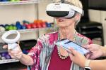A senior woman wearing a virtual-reality headset raises a controller in her right hand.