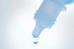 Close-up of eye drop bottle showing a drip with a white background