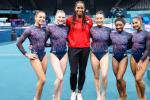 Marcia Faustin wearing red shirt and black pants. She is standing between five female gymnasts wearing the U.S. official leotards to the Olympics.