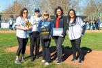 Five people stand on baseball field, with one person holding a certificate and one person holding an AED in a bag.  