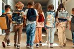 7 children standing side by side wearing backpacks in school hallway