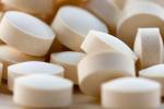 A close-up view of a pile of cream-colored round pills on a flat surface. 