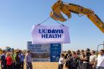 A construction worker uses a large crane to lift up a sign that says “UC Davis Health” to unveil a large sign 
