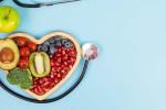 Fruit and vegetables in a wooden heart-shaped box next to a stethoscope and an apple.