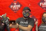 Three people wearing face masks pose in front of a Fuego 103.5 radio station banner.