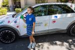 Young female with a green painted hand standing next to a car with handprints