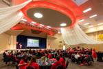 Guests gather in a large event hall decorated in red and white as they listen to a speaker during a heart‑health forum.