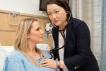 Doctor listening to patient’s heartbeat as she lays in hospital bed