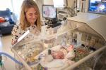 Woman looks over baby in NICU isolette.